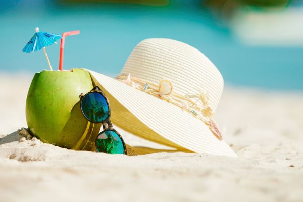 Eine frisch aufgeschlagene Kokosnuss, eine Sonnenbrille und ein Sonnenhut liegen am Strand.