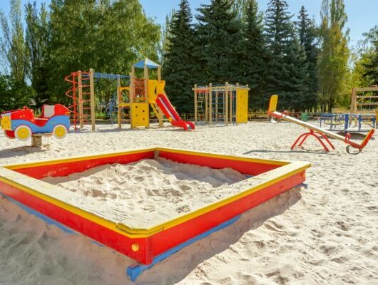 Colorful playground with slides, swings, and a red sandbox surrounded by trees.