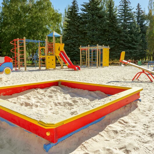 Colorful playground with slides, swings, and a red sandbox surrounded by trees.