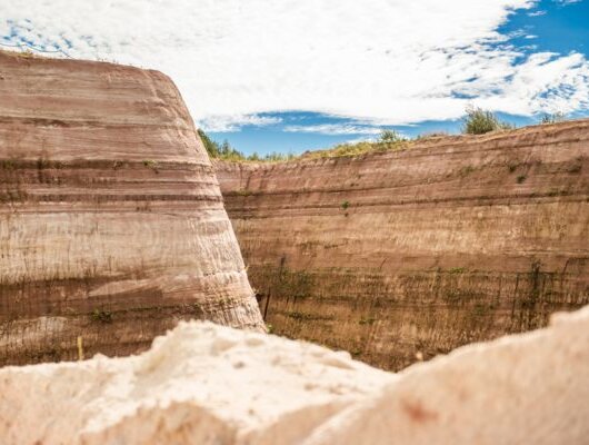 Steep, layered sandstone walls of a sand pit under a blue sky with light clouds.