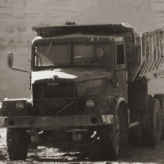 Vintage dump truck in a sand pit, photographed in sepia tones, symbolizing early sand extraction work.