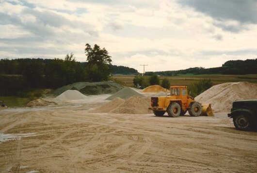 Construction site in a rural area with a yellow wheel loader and piles of sand and gravel.