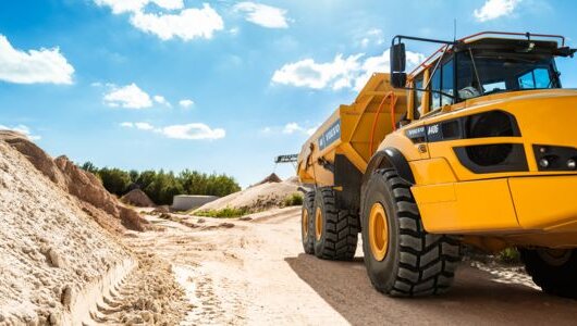 Large yellow dump truck on a bright sand road under a blue sky, representing modern sand quarry operations.