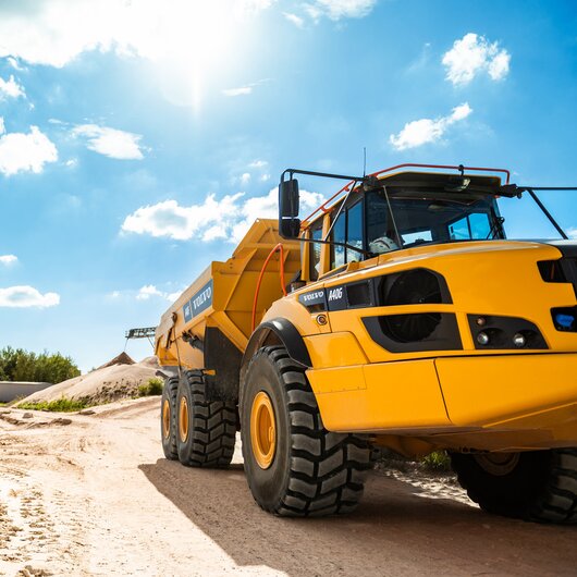 Large yellow dump truck on a bright sand road under a blue sky, representing modern sand quarry operations.