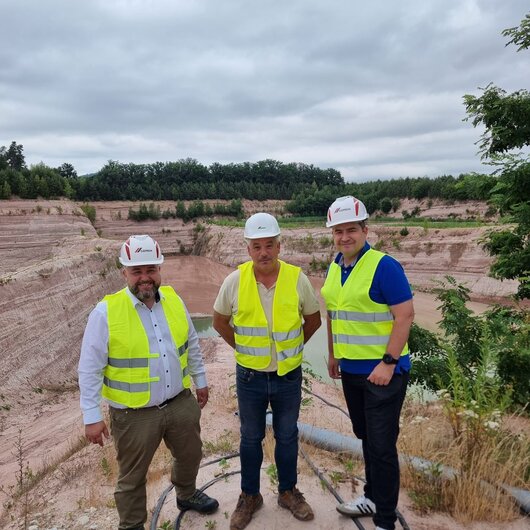 Three men wearing hard hats and safety vests in a sand quarry