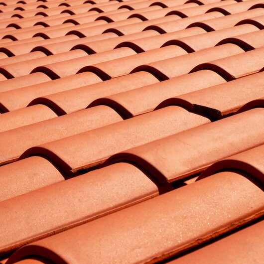 Close-up of a roof with evenly arranged reddish-brown clay tiles.