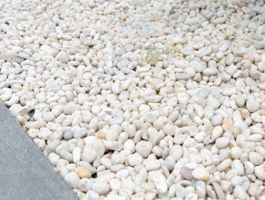 Area of smooth white decorative pebbles beside a gray stone edge.