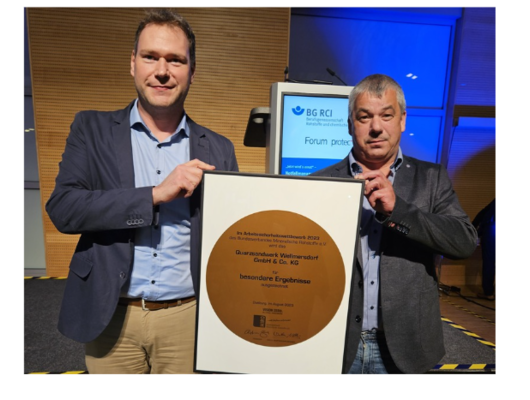Two men hold a large certificate recognizing outstanding occupational safety achievements of the Wellmersdorf quartz sand plant.