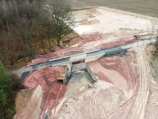 Aerial view of a sand quarry with a newly built concrete bridge, surrounded by forest and agricultural fields.