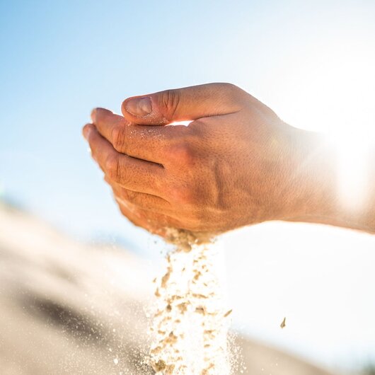 Hands letting sand run through fingers in sunlight