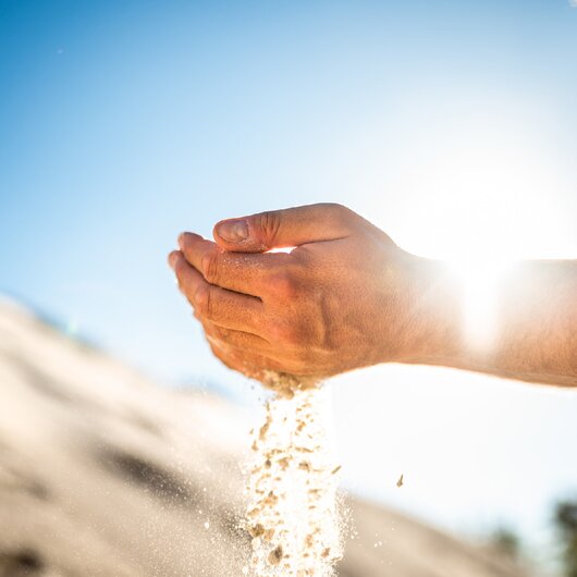 Hands letting sand run through fingers in sunlight